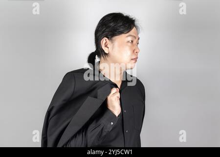 Asiatischer Mann in schwarzem Anzug steht vor hellgrauem Hintergrund. Stockfoto