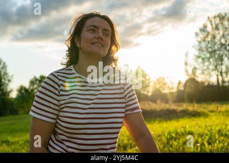 Eine Frau entspannt sich auf einer sonnendurchfluteten Wiese mit einem ruhigen Ausdruck. Stockfoto