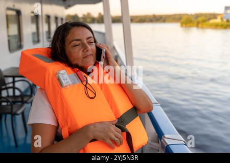 Frau in einer Schwimmweste, die ein Telefongespräch auf einem Boot genießt. Stockfoto