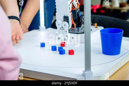 Roboter-automatische Hand nimmt Würfel und setzt Glas ein. Automatischer Roboterarm, der die Farbe des Würfels unterscheidet und in Glas derselben Farbe einsetzt. Automatisierung, moderne Technologien. Künstliche Intelligenz Stockfoto