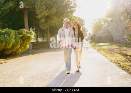 Ein Paar schlendert Hand in Hand durch einen sonnigen Park und teilt süße, fröhliche Momente Stockfoto