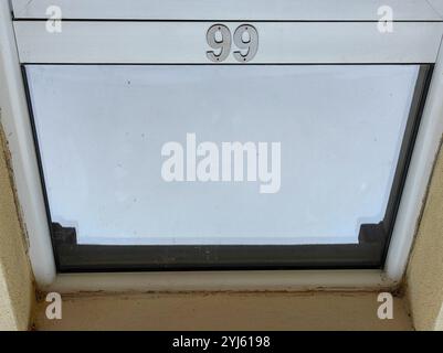 Nummer 99 auf Glastürrahmen, isoliert im negativen Raum mit Himmelsreflektion Stockfoto