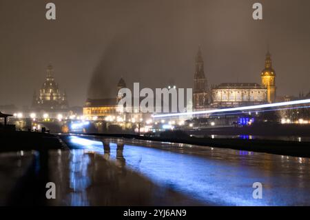 Dresden, Deutschland. November 2024. Die historische Altstadt mit der Frauenkirche (l-r), dem Ständehaus, dem Rathaus, der Hofkirche und dem Hausmannsturm ist abends im Dunst des Regens zu sehen. (Aufgenommen mit einer langen Belichtungszeit, die Lichtstreifen wurden durch die Lichter von Radfahrern erzeugt) Credit: Robert Michael/dpa/Alamy Live News Stockfoto