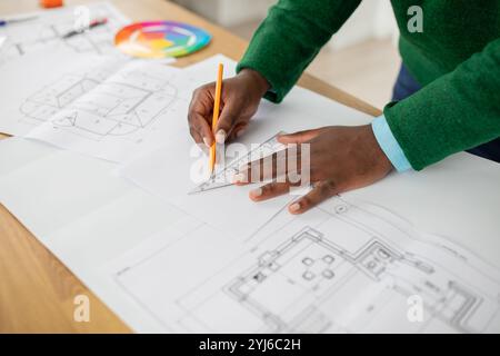 Eine Person konzentriert sich darauf, architektonische Pläne mit einem Lineal und Bleistift auf einem Holztisch zu entwerfen. Farbmuster sind sichtbar, was darauf hinweist, dass DE beachtet wird Stockfoto