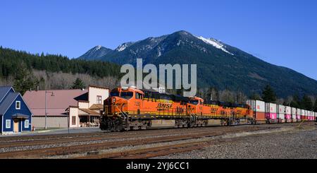 Skykomish, WA, USA - 6. November 2024; BNSF-intermodaler Güterzug fährt über Skykomish und schneebedeckten Gipfel Stockfoto