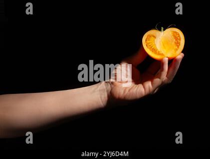 In Scheiben geschnittene gelbe Tomate in der Hand auf schwarzem Hintergrund Stockfoto