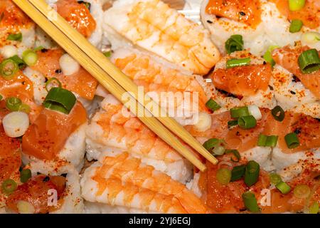 Nahaufnahme eines Tellers Sushi mit Lachs-Nigiri, Garnelen-Nigiri und einem Paar Essstäbchen. Das Sushi wird mit grünen Zwiebeln und rotem Chili belegt Stockfoto