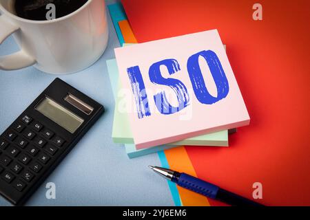 ISO. Notizblock mit Text, Kaffeetasse und Taschenrechner und Schreibwaren auf Bürotisch. Stockfoto
