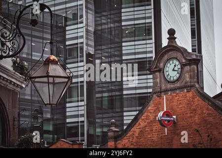 Eine hängende Laterne befindet sich vor einem modernen Wolkenkratzer, ein rotes Backsteingebäude mit einem Uhrenturm und unterirdischen Schildern sind im Vordergrund Stockfoto