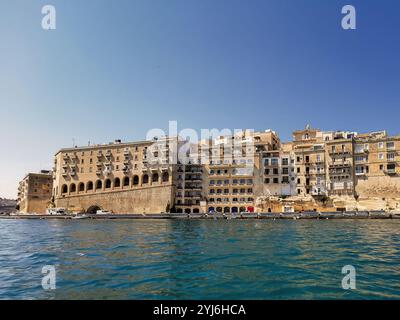 Historische Gebäude am Wasser in Senglea, Malta, mit Blick auf das klare blaue Meer unter hellem Himmel. Stockfoto