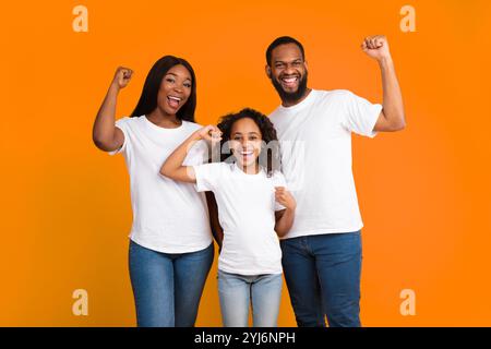 Ja. Porträt einer aufgeregten jungen schwarzen Familie von drei Leuten, die geballte Fäuste schütteln und Siegergesten machen. Glücklicher Afroamerikaner, Mann, Frau und Mädchen Stockfoto