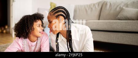 Afroamerikanische Mutter und Tochter treten auf dem Boden ihres gemütlichen Wohnzimmers spielerisch und liebevoll auf und unterstreichen die Wärme von Stockfoto