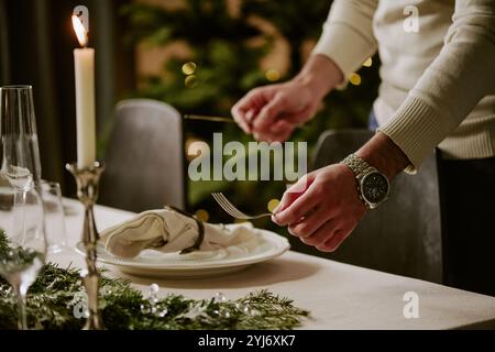 Mittlere Nahaufnahme von nicht erkennbaren männlichen Händen, die polierte silberne Gabel und Messer halten, während sie Weihnachtstisch servieren Stockfoto