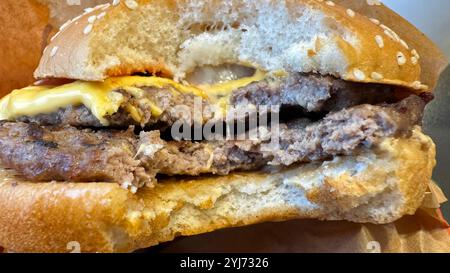 Eine Nahaufnahme eines doppelten Cheeseburgers, teilweise gegessen, mit zwei Rindfleischpasteten, geschmolzenem Käse und einem Sesambrötchen. Das Brötchen ist leicht kompakt Stockfoto