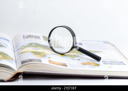 Lupe auf offenem Buch symbolisiert Suche, Forschung und tiefgreifende Erforschung von Wissen und Informationen, betont Entdeckung und Detailgenauigkeit Stockfoto