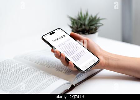 Telefon in Hand, das die App für die Buchübersetzung mit OCR-Scankonzept anzeigt. Ideal für Themen wie Sprachenlernen, Übersetzungstechnologie, Lesen und d Stockfoto