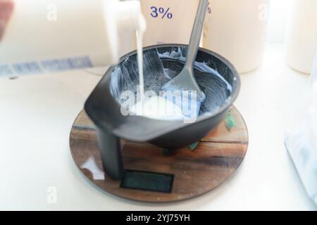 Eine Frau mischt die Haarfarbe in einem Friseursalon mit präzisen Messungen und Werkzeugen, um die perfekte Formel zu erzielen. Der Arbeitsbereich ist organisiert und präsentiert Stockfoto