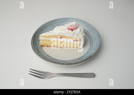 Ein kleiner japanischer Erdbeer-Shortcake und eine kleine Gabel auf einem stilvollen japanischen Teller auf einem weißen Tisch. Stockfoto