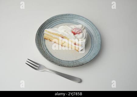 Ein kleiner japanischer Erdbeer-Shortcake und eine kleine Gabel auf einem stilvollen japanischen Teller auf einem weißen Tisch. Stockfoto