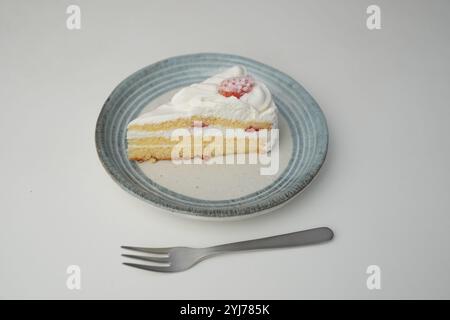 Ein kleiner japanischer Erdbeer-Shortcake und eine kleine Gabel auf einem stilvollen japanischen Teller auf einem weißen Tisch. Stockfoto