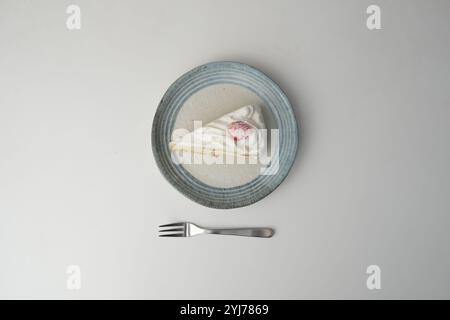 Ein kleiner japanischer Erdbeer-Shortcake und eine kleine Gabel auf einem stilvollen japanischen Teller auf einem weißen Tisch. Stockfoto