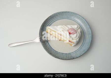 Ein kleiner japanischer Erdbeer-Shortcake und eine kleine Gabel auf einem stilvollen japanischen Teller auf einem weißen Tisch. Stockfoto