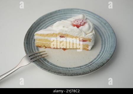 Ein kleiner japanischer Erdbeer-Shortcake und eine kleine Gabel auf einem stilvollen japanischen Teller auf einem weißen Tisch. Stockfoto