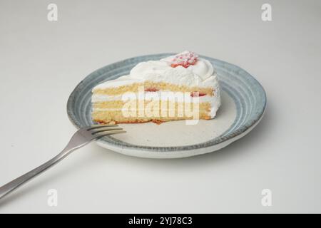 Ein kleiner japanischer Erdbeer-Shortcake und eine kleine Gabel auf einem stilvollen japanischen Teller auf einem weißen Tisch. Stockfoto