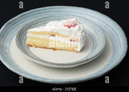 Ein kleiner japanischer Erdbeerkuchen auf zwei stilvollen überlappenden großen und kleinen Tellern im japanischen Stil auf einem schwarzen Tuch auf einem weißen Tisch. Stockfoto