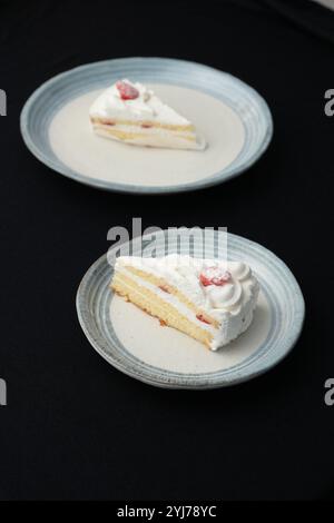 Kleine japanische Erdbeer-Shortcakes auf zwei stilvollen japanischen Tellern, jeweils auf einem schwarzen Tuch auf einem weißen Tisch. Stockfoto