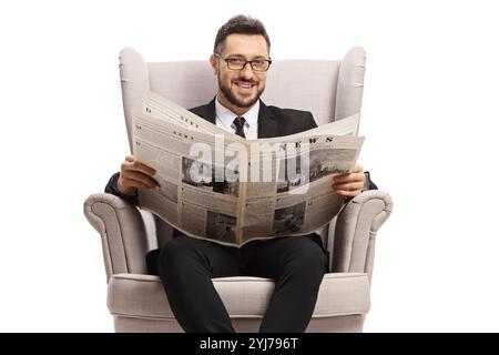 Gutaussehender Mann in einem Sessel, der eine Zeitung hält und auf weißem Hintergrund lächelt Stockfoto