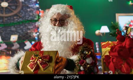 Saint Nick packt eine Geschenkbox in seiner Werkstatt, umgeben von festlichen Dekorationen. Dekorieren Sie die Geschenke mit schönen Ornamenten für den Weihnachtsgeist, und reisen Sie um den Heiligabend herum um die Welt. Kamera A.. Stockfoto