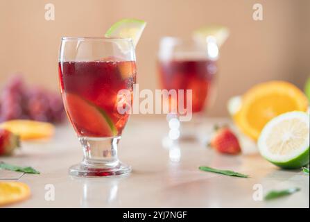 Nahaufnahme von Glasbechern mit hausgemachtem Sommerwein im Vordergrund vor dem Hintergrund von Orangen, Erdbeeren und Zitronen auf Keramiktisch Stockfoto