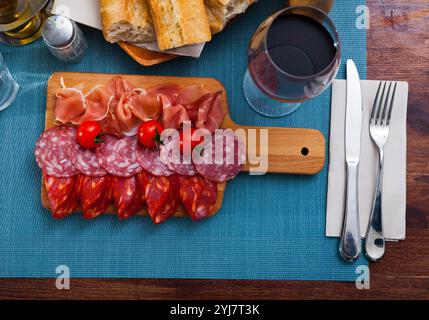 Spanische leckere Gerichte, die Würstchen und Schinken mit Tomaten am Holzschreibtisch schneiden Stockfoto