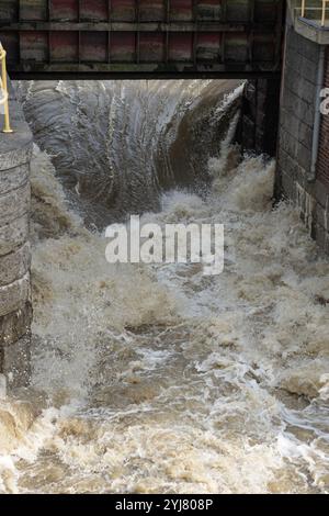 Starker Wasserfluss, der nach starkem Regen durch die Schleusen des Staudamms strömt und intensive Strömungen und schaumige Wellen erzeugt Stockfoto