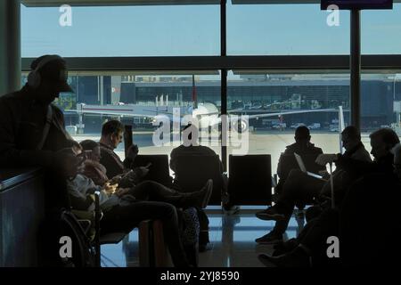 Flughafen London Heathrow, London, Großbritannien 12. November 2024 Passagiere/Reisende (in Silhouette) verwenden ihre Mobilgeräte, während sie auf ihren Flug warten Stockfoto