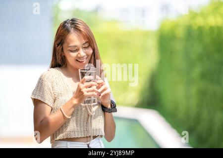 Asiatische Frau hält ein Glas Wasser aus dem Trinken auf Outdoor-Feld mit Bokeh grünen Banner Hintergrund. Stockfoto