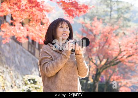 Eine Frau mittleren Alters fotografiert Herbstlaub mit einer Kamera Stockfoto