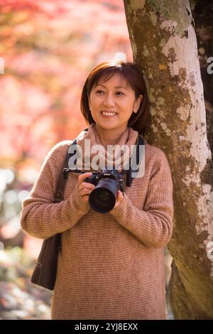 Eine Frau mittleren Alters fotografiert Herbstlaub mit einer Kamera Stockfoto