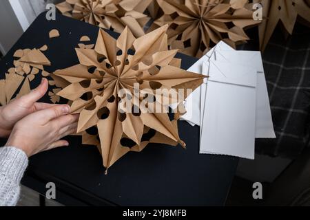 Nachhaltiges Weihnachtsgemütliches, handgefertigtes Dekor. Tutorial für die Herstellung von „Do IT Yourself“-Papiertüten und Heißkleber. Saisonale Aktivität für Kinder. 3D-Schneeflocken Vorbereitung am Weihnachtsabend Stockfoto