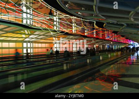 Passagiere, die sich zwischen den Terminals am Chicago O'Hare International Airport bewegen, laufen unter einem farbenfrohen Neonlicht über dem People Mover Stockfoto
