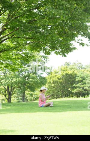 Frau mit weißem Hut, die ein Tablet im Park ansieht Stockfoto