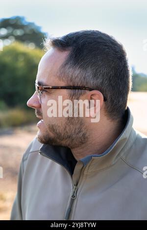 Profilporträt eines jungen Mannes mit Bart und Brille, der draußen auf der Straße steht Stockfoto