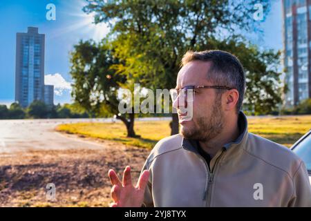 Profilporträt eines Immobilienmaklers, alleinstehender junger Mann mit Bart und Brille, der draußen auf der Straße steht, Wohngebiet Stockfoto