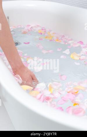 Frauenhand schöpft Blumenblätter in Badewannenwasser Stockfoto