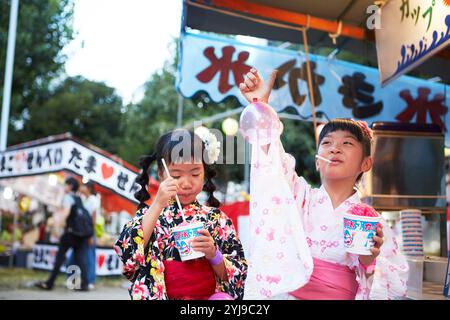 Ein Mädchen in Yukata isst rasiertes Eis, das von einem Festivalstand gekauft wurde Stockfoto