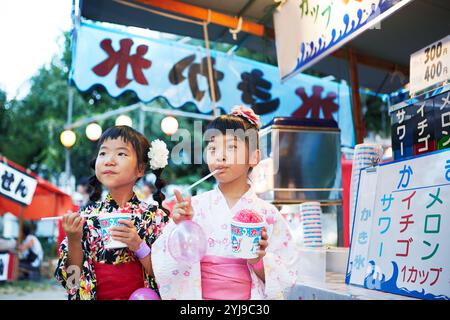 Ein Mädchen in Yukata isst rasiertes Eis, das von einem Festivalstand gekauft wurde Stockfoto