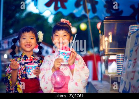 Ein Mädchen in Yukata isst rasiertes Eis, das von einem Festivalstand gekauft wurde Stockfoto