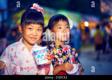 Ein Mädchen in Yukata isst rasiertes Eis, das von einem Festivalstand gekauft wurde Stockfoto