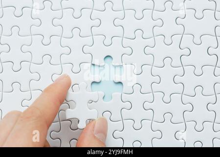 Die Hand hält eines der Teile eines leeren weißen Puzzles Stockfoto